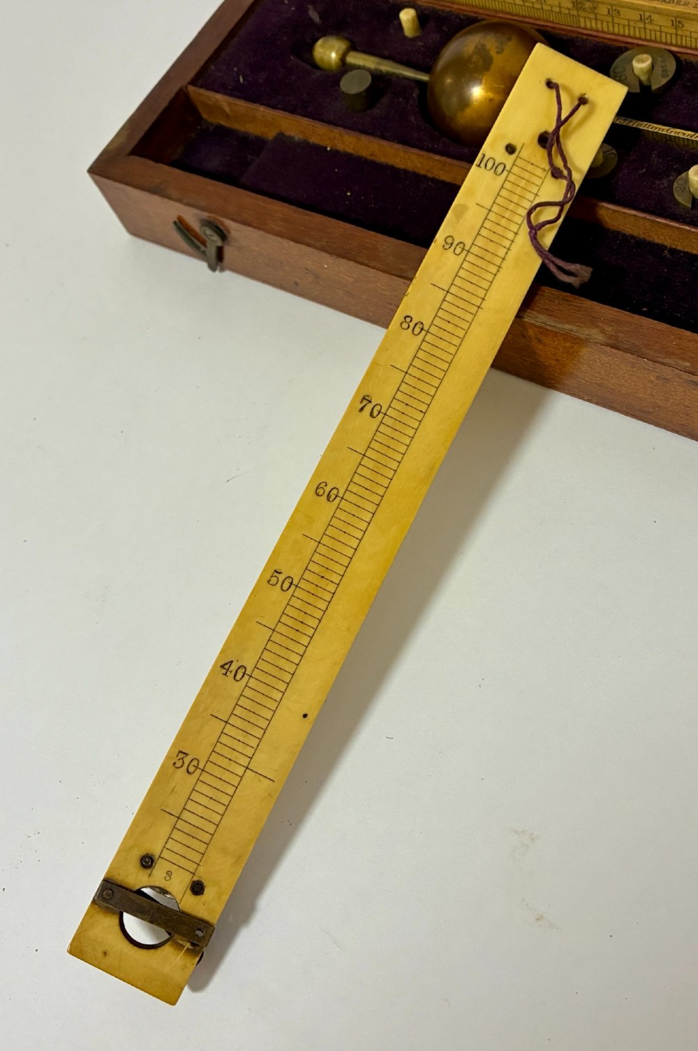 A Victorian Sikes hydrometer set resting inside an open fitted mahogany box lined with purple velvet, containing a brass float, slotted weights, and a thermometer. View X