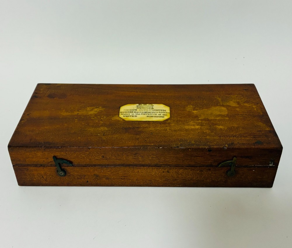 A Victorian Sikes hydrometer set resting inside an open fitted mahogany box lined with purple velvet, containing a brass float, slotted weights, and a thermometer. View XI