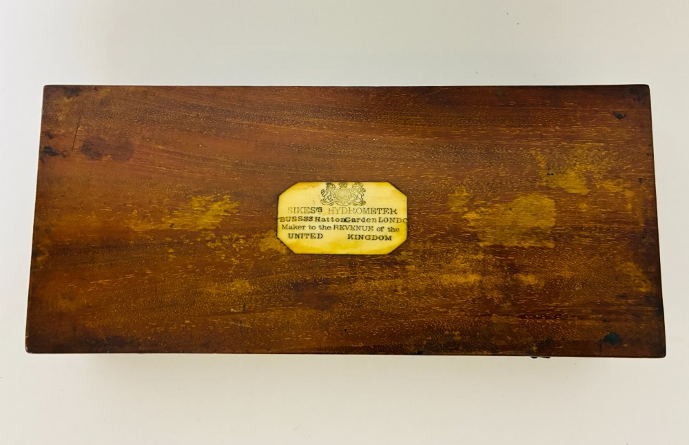 A Victorian Sikes hydrometer set resting inside an open fitted mahogany box lined with purple velvet, containing a brass float, slotted weights, and a thermometer. View XII