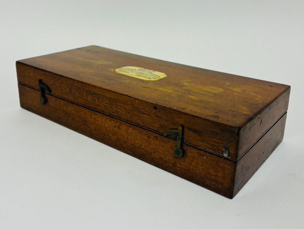 A Victorian Sikes hydrometer set resting inside an open fitted mahogany box lined with purple velvet, containing a brass float, slotted weights, and a thermometer. View XIV