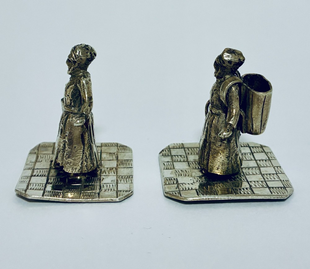 A pair of miniature silver figures depicting figures with a bucket and a walking stick on square patterned bases. View II