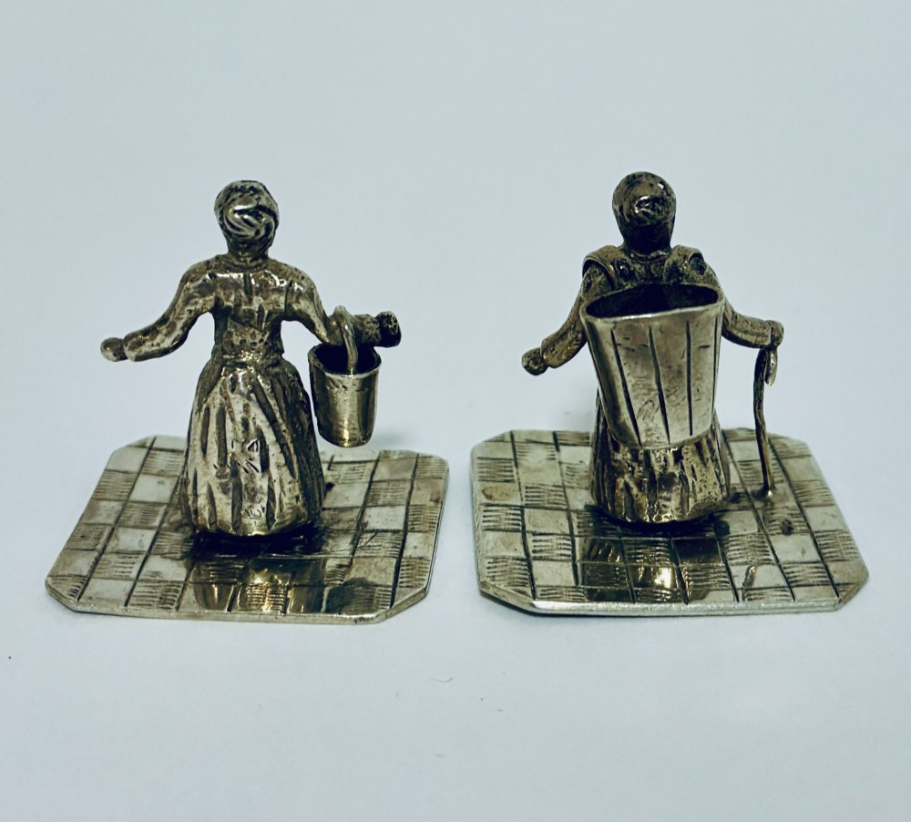 A pair of miniature silver figures depicting figures with a bucket and a walking stick on square patterned bases. View III
