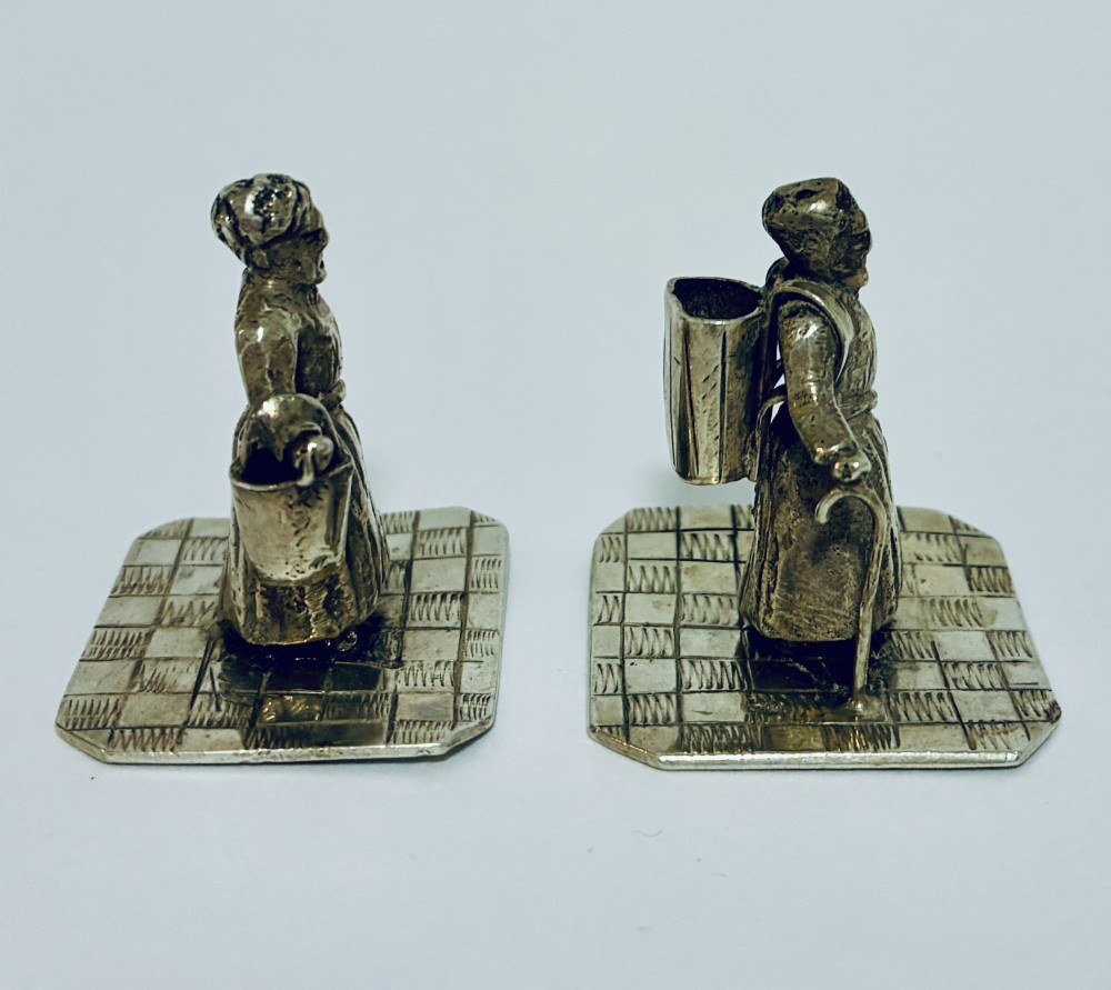 A pair of miniature silver figures depicting figures with a bucket and a walking stick on square patterned bases. View IV