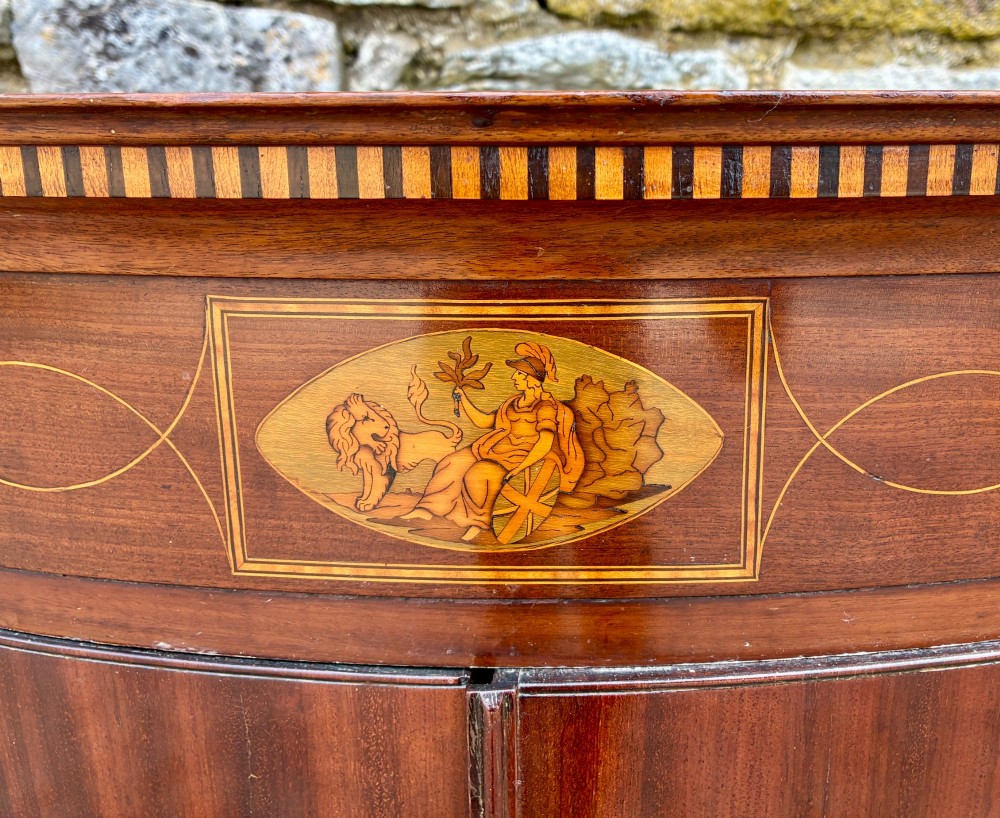 A Georgian bow-front mahogany corner cupboard featuring detailed marquetry inlays, decorative brass hinges, and central keyhole escutcheons. View IV