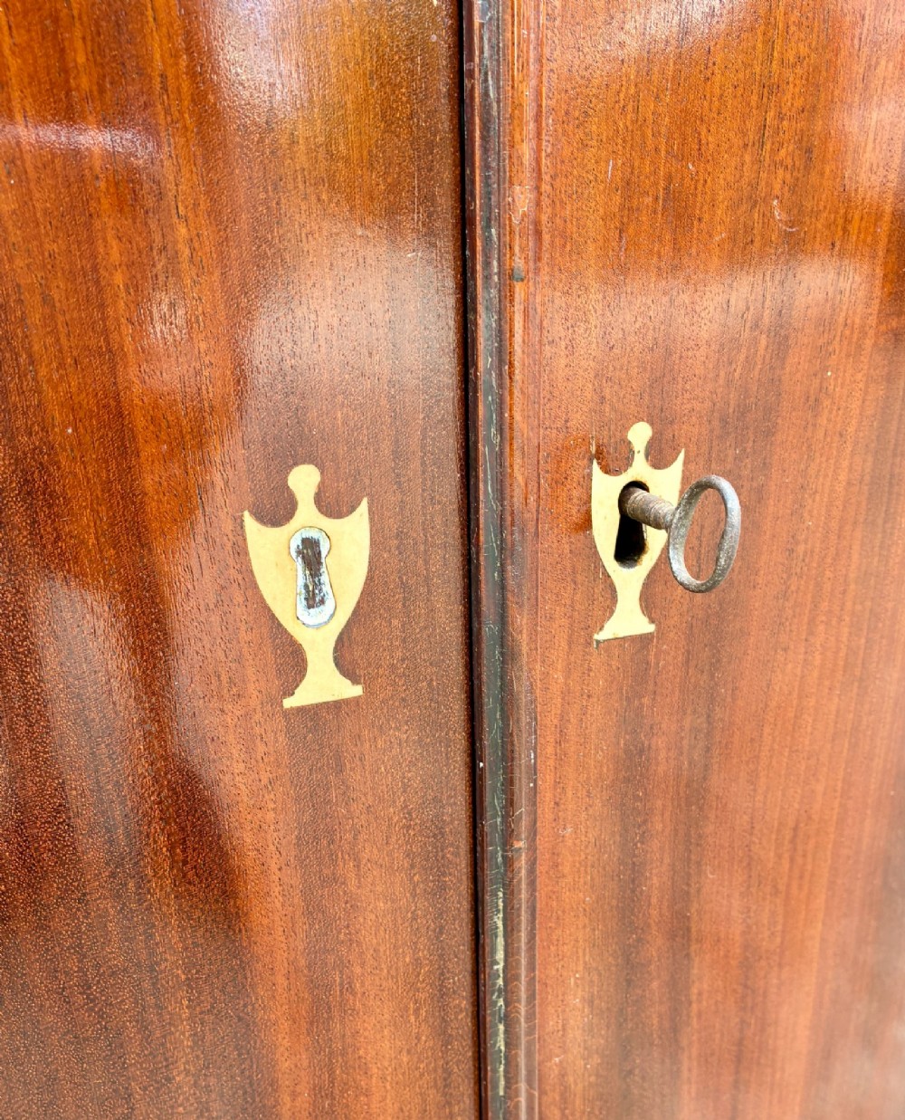 A Georgian bow-front mahogany corner cupboard featuring detailed marquetry inlays, decorative brass hinges, and central keyhole escutcheons. View VII