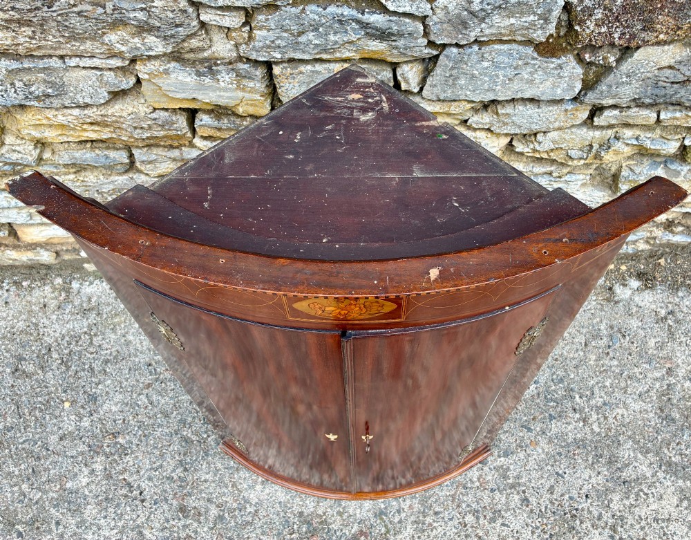 A Georgian bow-front mahogany corner cupboard featuring detailed marquetry inlays, decorative brass hinges, and central keyhole escutcheons. View VIII