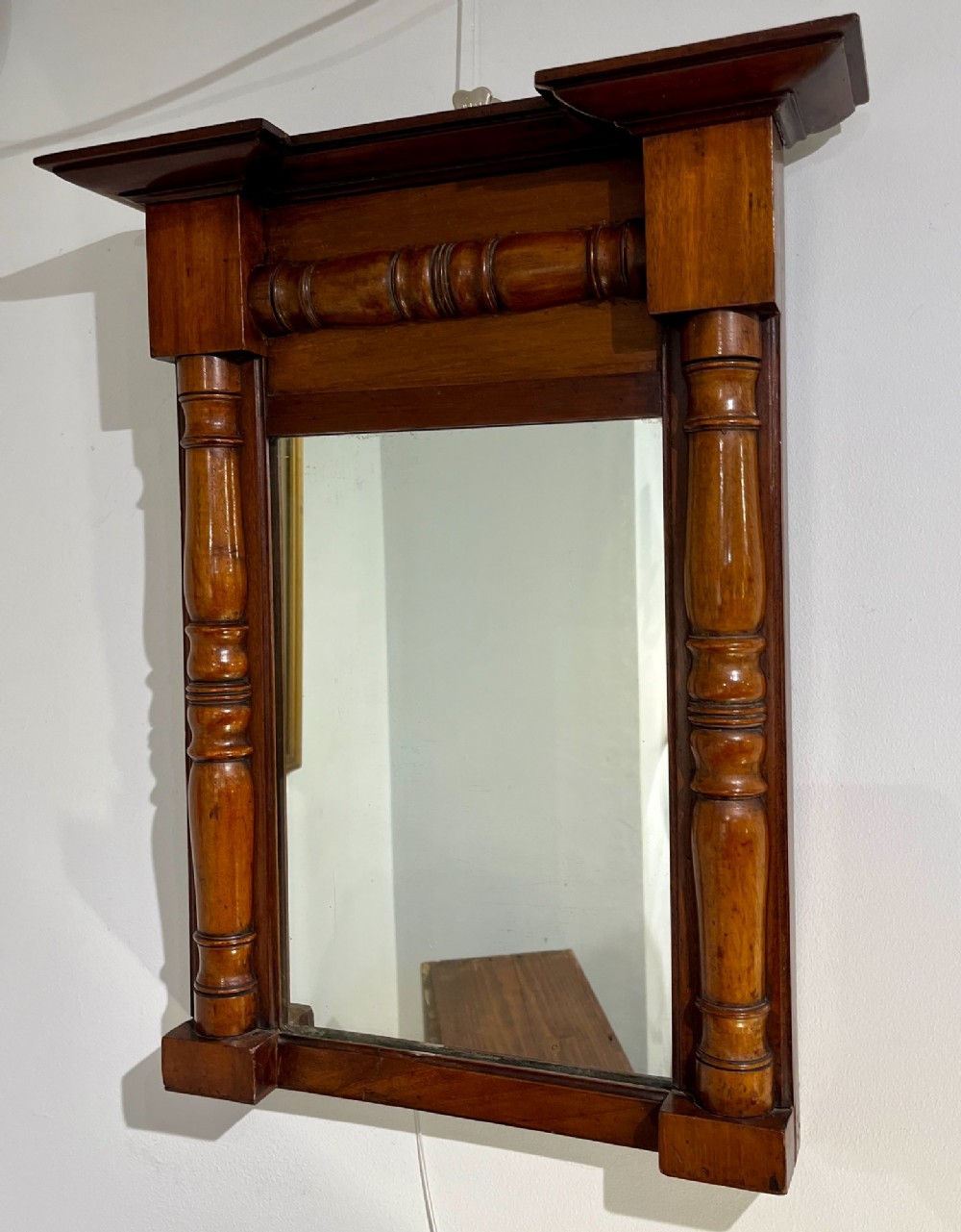 A vertical antique mahogany pier mirror featuring turned column pilasters on either side and a protruding moulded top cornice.