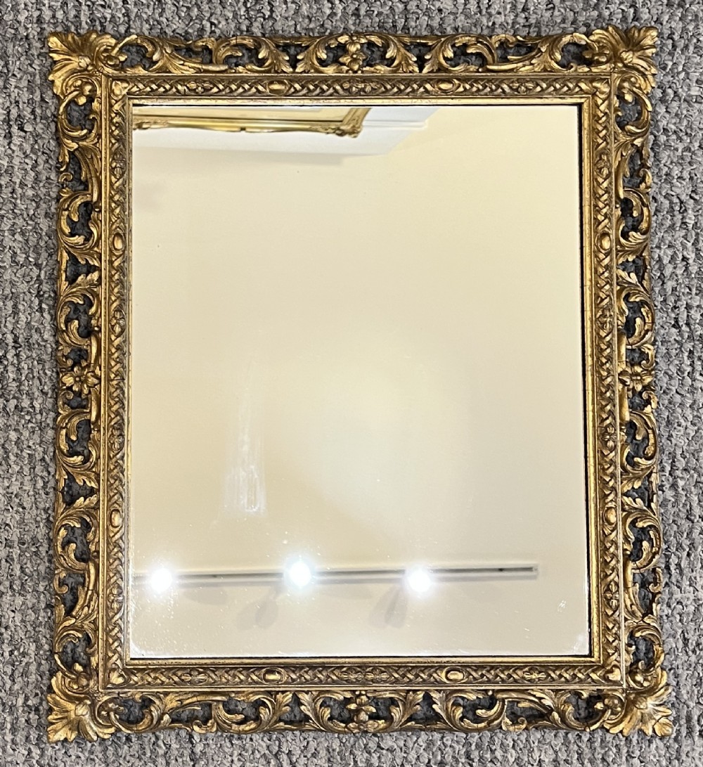 A rectangular wall mirror featuring an ornate pierced giltwood frame decorated with carved acanthus leaf scrollwork and bead moulding.