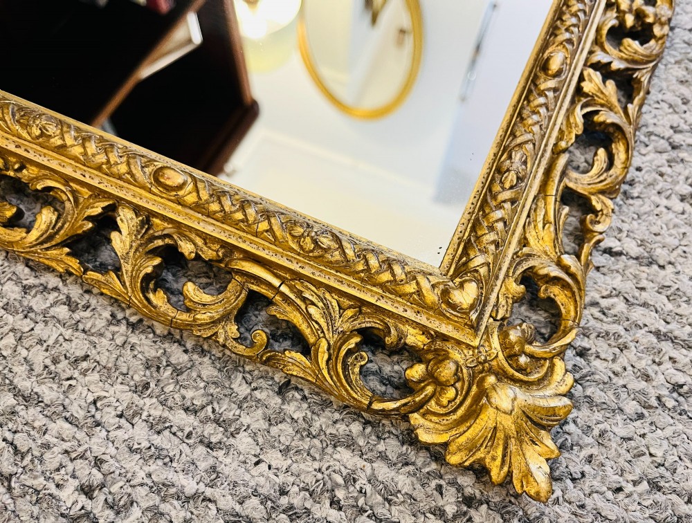 A rectangular wall mirror featuring an ornate pierced giltwood frame decorated with carved acanthus leaf scrollwork and bead moulding. View IV