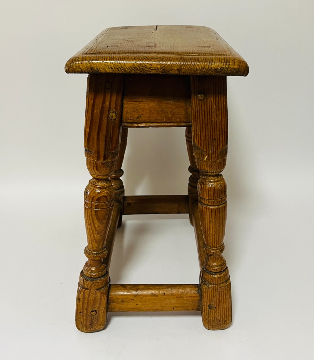 A low rectangular antique pine joint stool with turned legs, base stretchers, and visible wooden dowel construction. View III