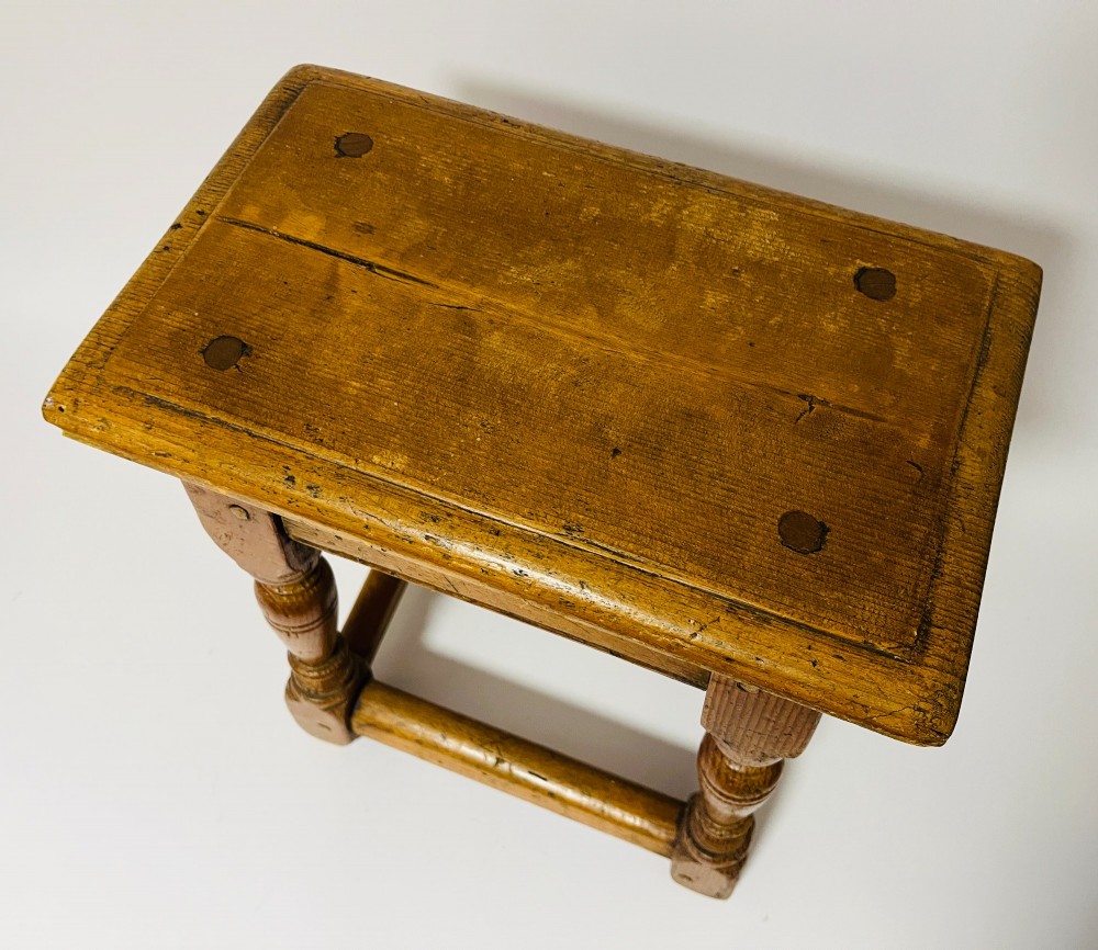 A low rectangular antique pine joint stool with turned legs, base stretchers, and visible wooden dowel construction. View V