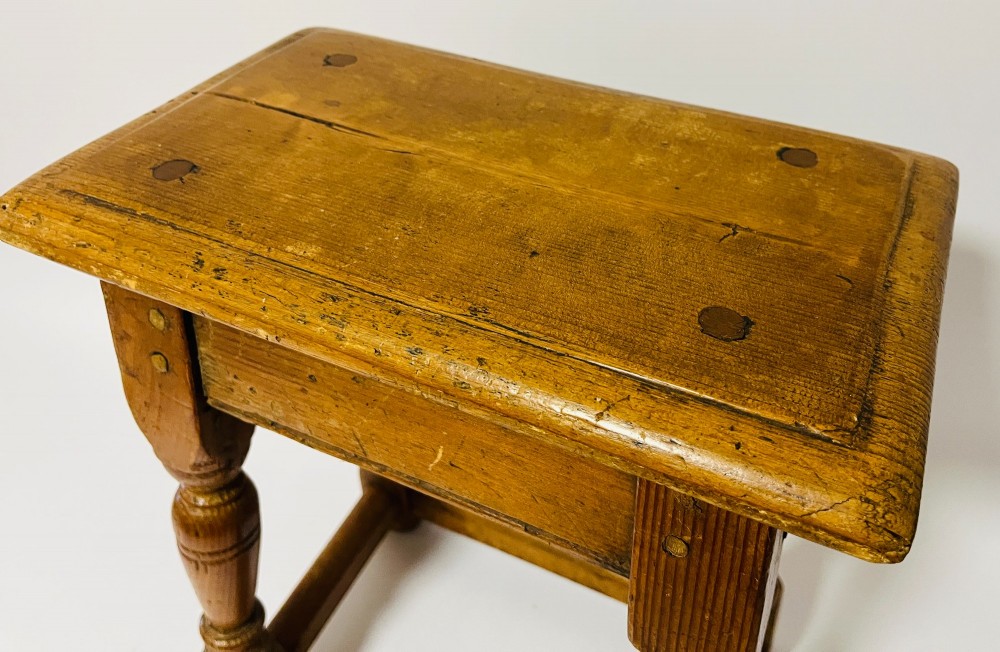 A low rectangular antique pine joint stool with turned legs, base stretchers, and visible wooden dowel construction. View VI