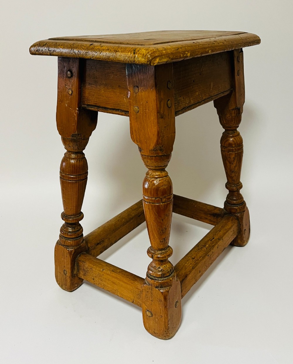 A low rectangular antique pine joint stool with turned legs, base stretchers, and visible wooden dowel construction. View VII