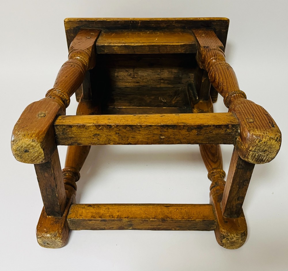 A low rectangular antique pine joint stool with turned legs, base stretchers, and visible wooden dowel construction. View X