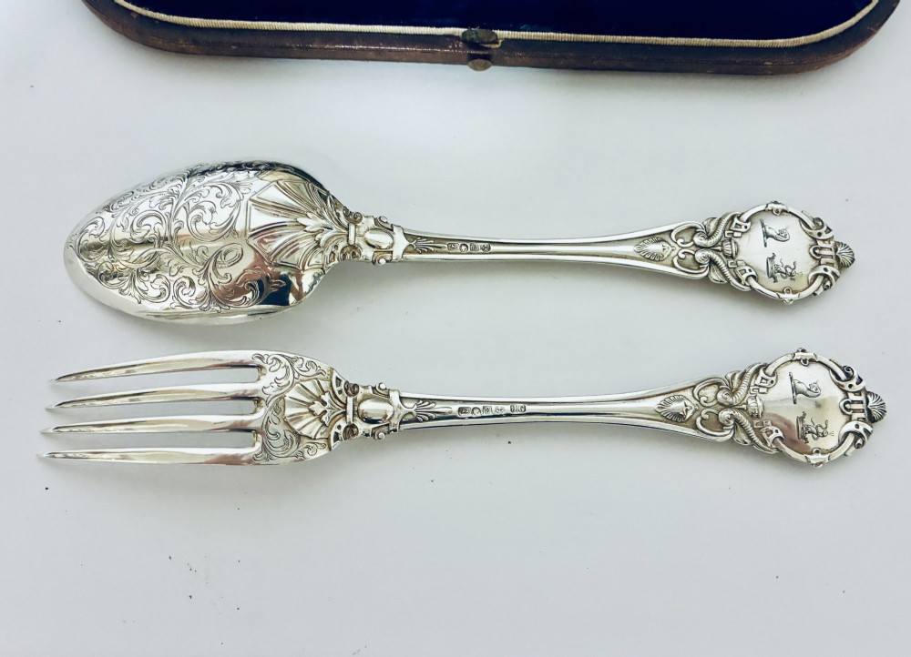 An antique Victorian silver christening spoon and fork with intricate foliate engraving, arranged inside a velvet-lined dark leather presentation case. View VI