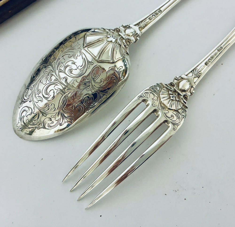 An antique Victorian silver christening spoon and fork with intricate foliate engraving, arranged inside a velvet-lined dark leather presentation case. View VII