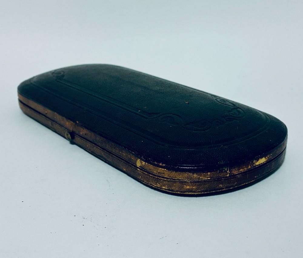 An antique Victorian silver christening spoon and fork with intricate foliate engraving, arranged inside a velvet-lined dark leather presentation case. View XI