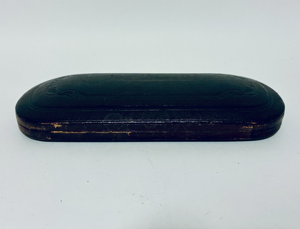 An antique Victorian silver christening spoon and fork with intricate foliate engraving, arranged inside a velvet-lined dark leather presentation case. View XII