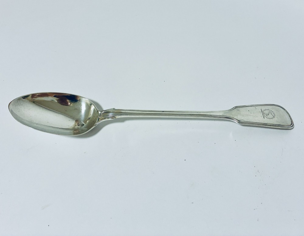 A Victorian silver serving spoon displaying a fiddle pattern handle with an engraved crest on the terminal.