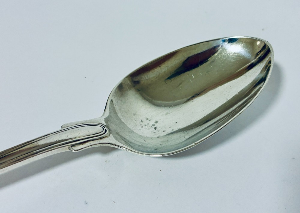 A Victorian silver serving spoon displaying a fiddle pattern handle with an engraved crest on the terminal. View IV