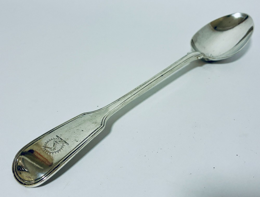 A Victorian silver serving spoon displaying a fiddle pattern handle with an engraved crest on the terminal. View V