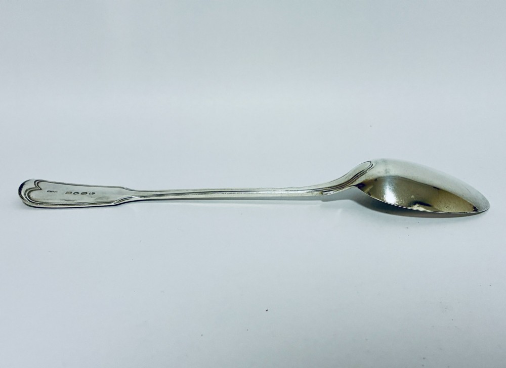 A Victorian silver serving spoon displaying a fiddle pattern handle with an engraved crest on the terminal. View VI