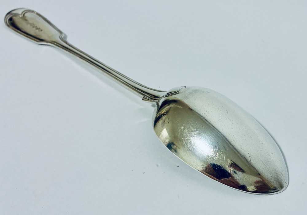 A Victorian silver serving spoon displaying a fiddle pattern handle with an engraved crest on the terminal. View VII