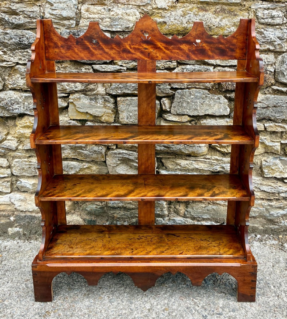 An Arts and Crafts satinwood open bookcase featuring four tiered shelves with a scalloped top gallery, shaped sides, and decorative pierced cut-outs.