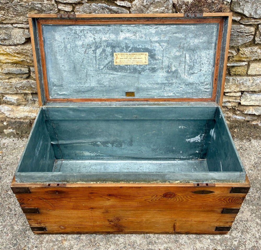 An antique rectangular pine campaign trunk with dark metal corner brackets, a brass escutcheon, and visible natural wood grain. View III