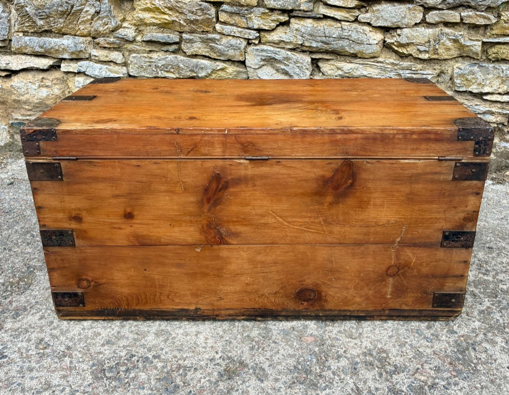An antique rectangular pine campaign trunk with dark metal corner brackets, a brass escutcheon, and visible natural wood grain. View XII