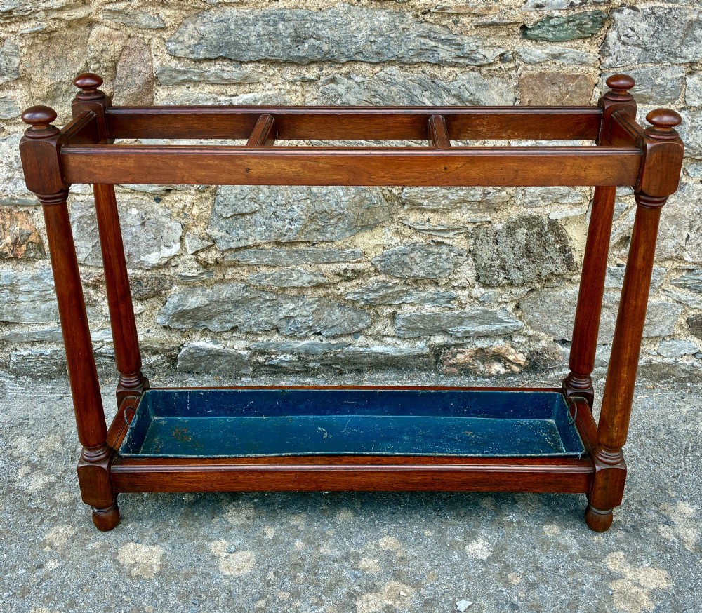 A Victorian mahogany umbrella stand with four divided top sections, turned support legs with ball finials, and a removable blue painted metal drip tray.