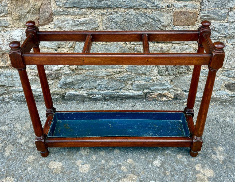 A Victorian mahogany umbrella stand with four divided top sections, turned support legs with ball finials, and a removable blue painted metal drip tray. View II