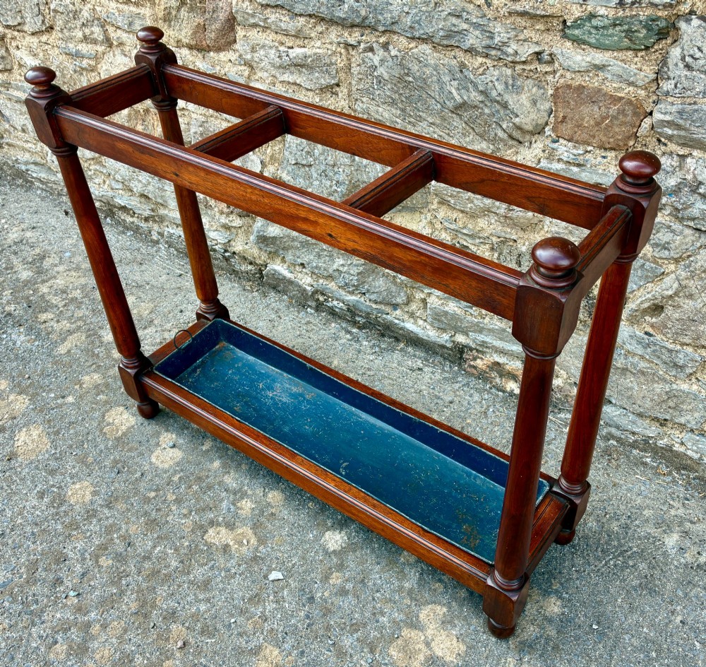 A Victorian mahogany umbrella stand with four divided top sections, turned support legs with ball finials, and a removable blue painted metal drip tray. View X