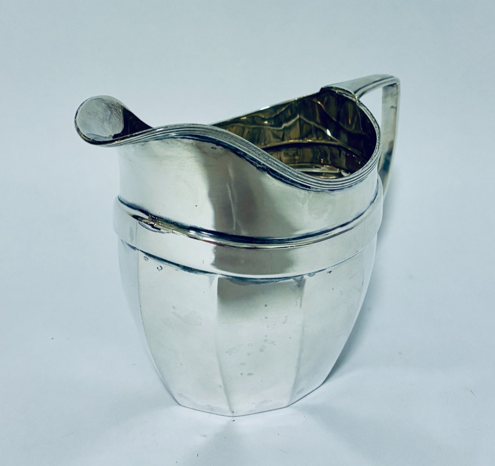 An antique polished silver milk jug featuring a faceted lower body, a shaped pouring spout with reeded rim, and an angular handle. View II
