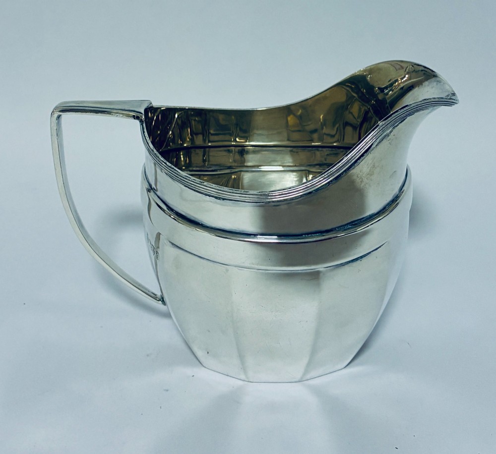 An antique polished silver milk jug featuring a faceted lower body, a shaped pouring spout with reeded rim, and an angular handle. View IV