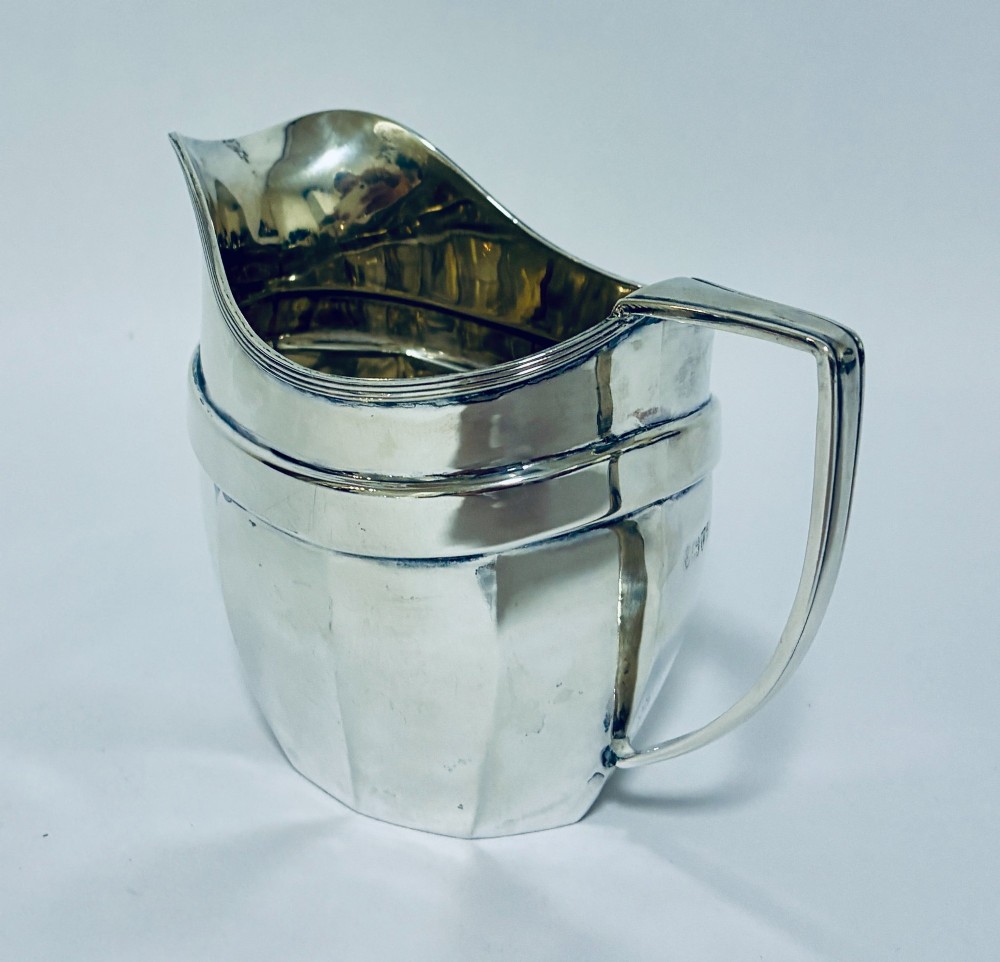 An antique polished silver milk jug featuring a faceted lower body, a shaped pouring spout with reeded rim, and an angular handle. View VII