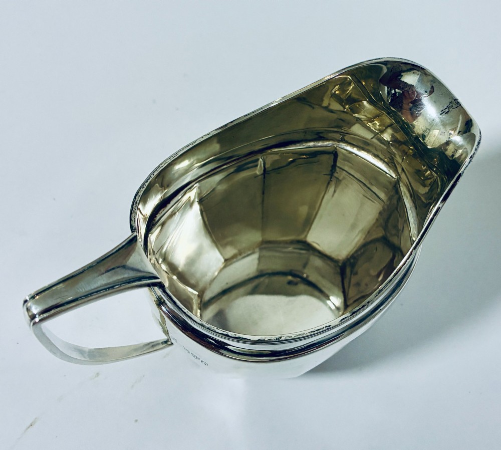 An antique polished silver milk jug featuring a faceted lower body, a shaped pouring spout with reeded rim, and an angular handle. View VIII