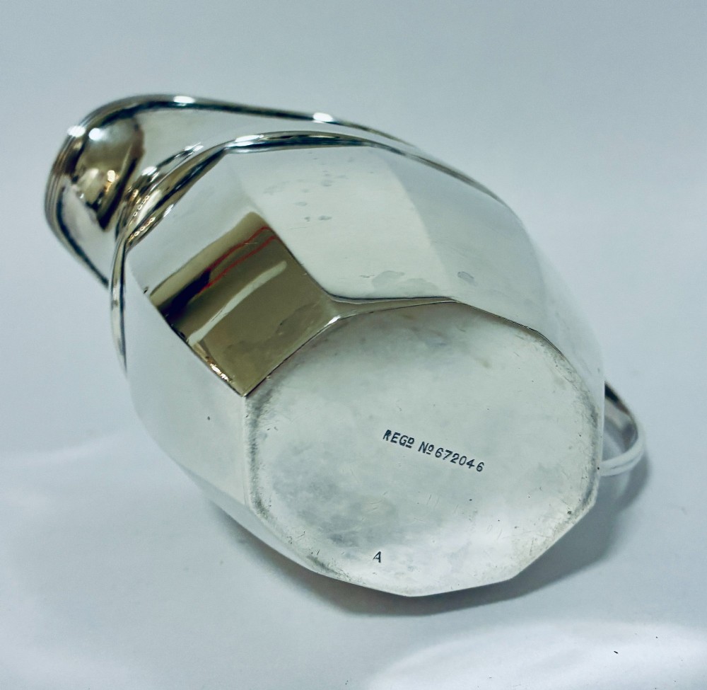 An antique polished silver milk jug featuring a faceted lower body, a shaped pouring spout with reeded rim, and an angular handle. View IX
