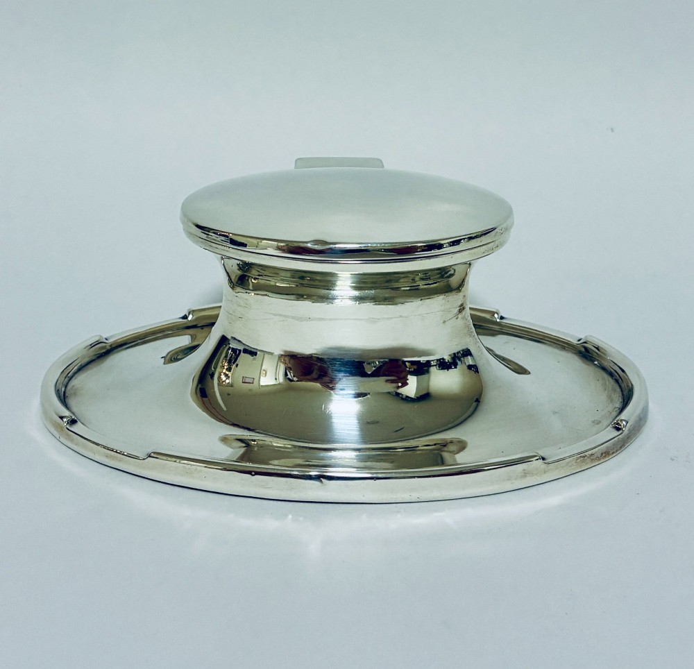 A solid silver capstan-shaped inkwell with a broad flared circular base and a hinged domed lid.