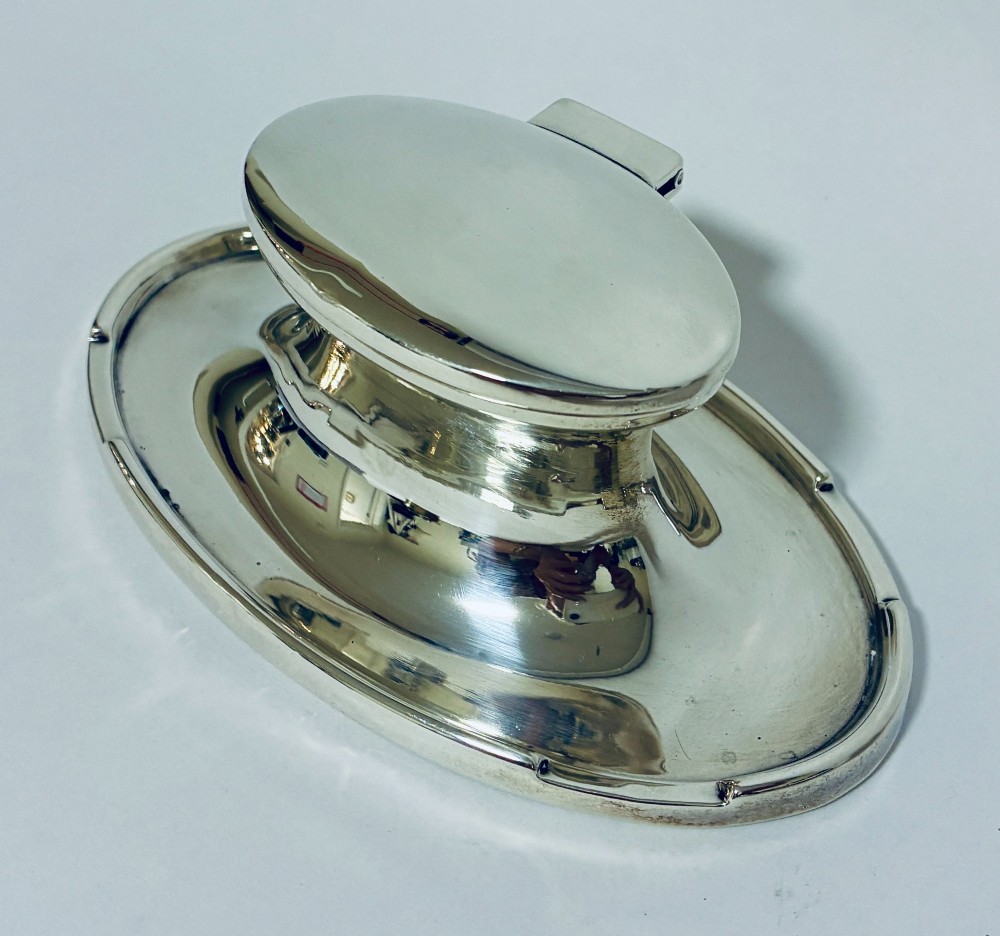 A solid silver capstan-shaped inkwell with a broad flared circular base and a hinged domed lid. View II