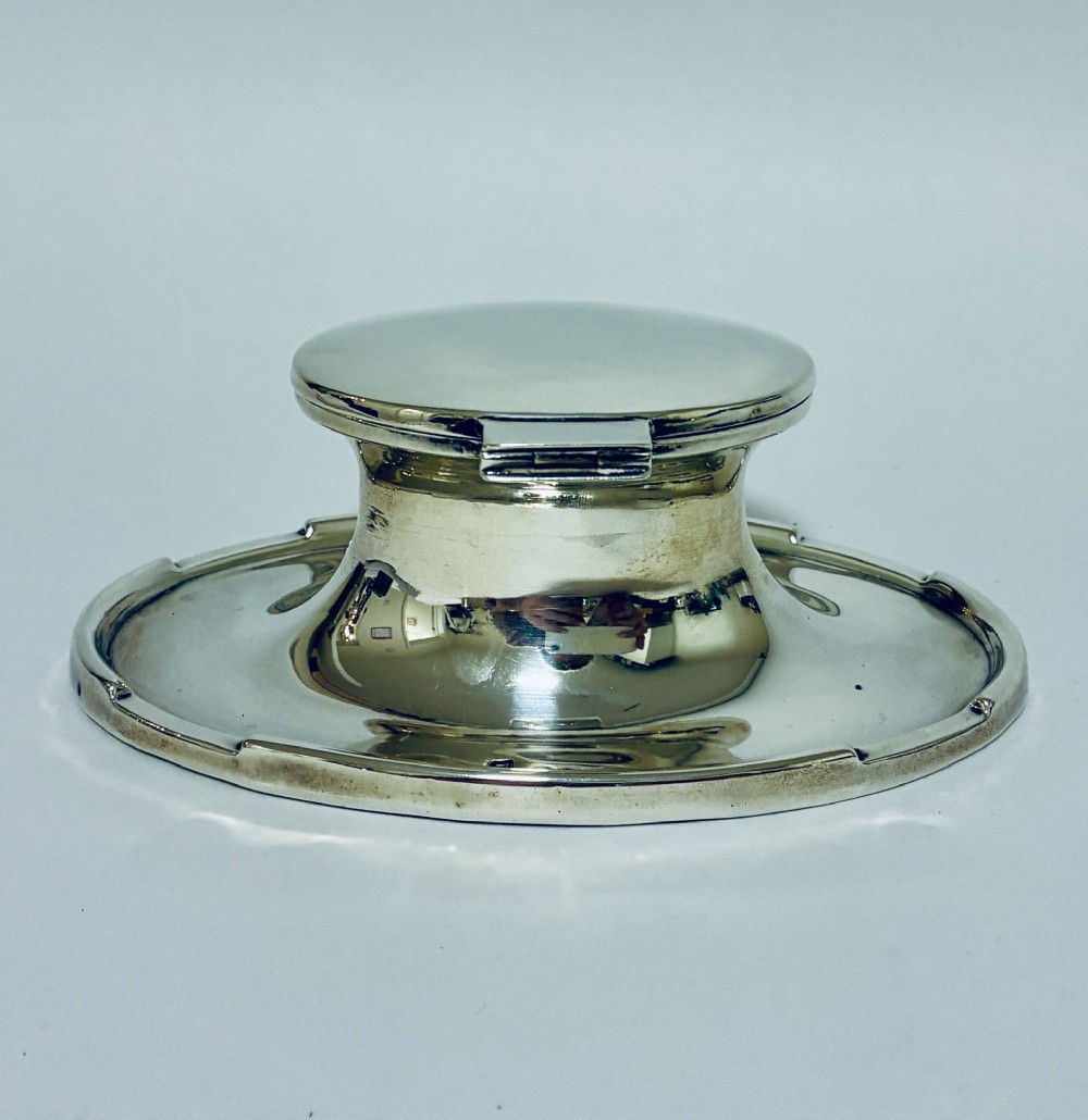 A solid silver capstan-shaped inkwell with a broad flared circular base and a hinged domed lid. View V
