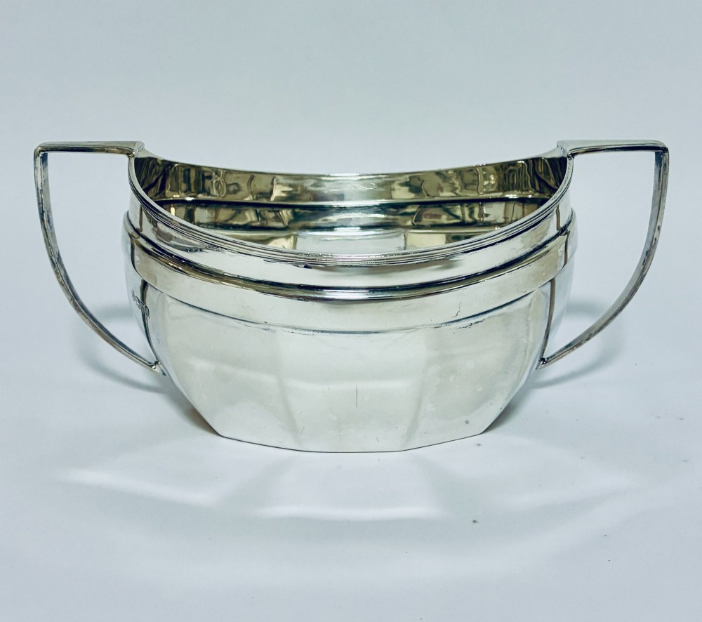 An antique silver twin-handled sugar bowl featuring angular handles, a faceted lower body, and visible hallmarks on the side.