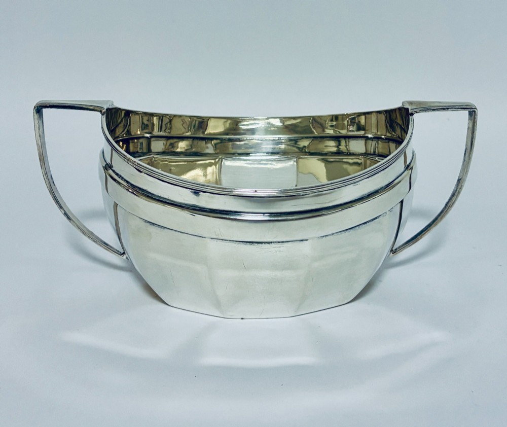 An antique silver twin-handled sugar bowl featuring angular handles, a faceted lower body, and visible hallmarks on the side. View V