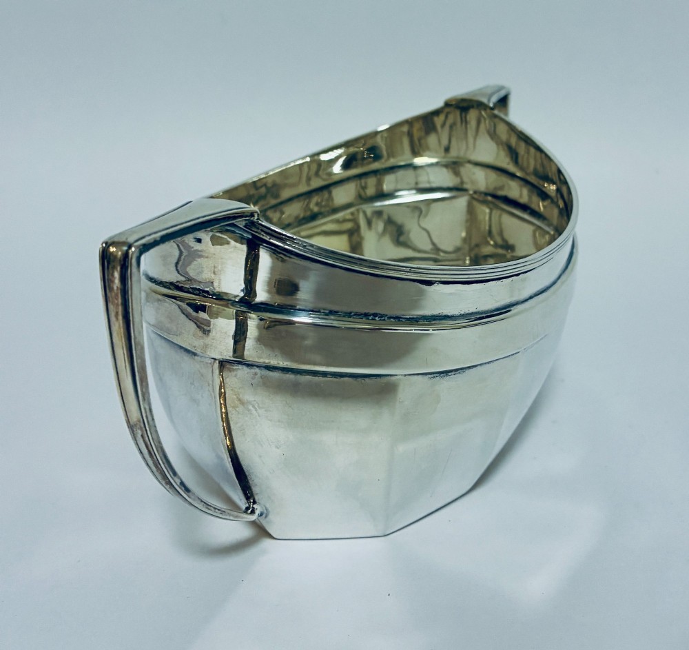 An antique silver twin-handled sugar bowl featuring angular handles, a faceted lower body, and visible hallmarks on the side. View VI