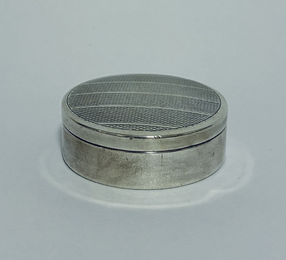 A round antique silver pill box featuring engine-turned geometric patterns on the lid.