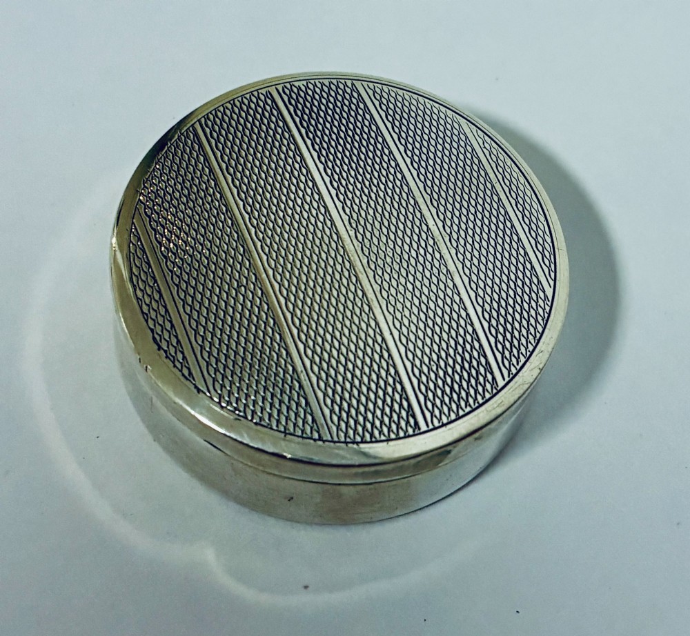 A round antique silver pill box featuring engine-turned geometric patterns on the lid. View II