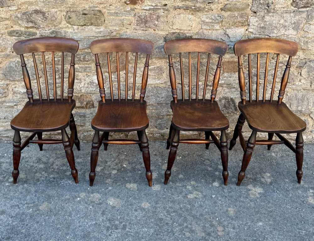 A set of four dark brown Victorian wooden kitchen chairs featuring spindle backs, shaped seats, and turned legs.