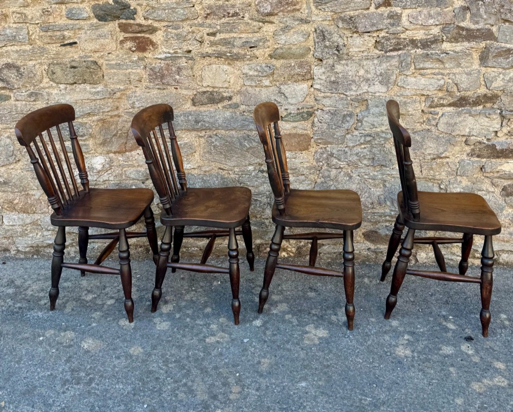A set of four dark brown Victorian wooden kitchen chairs featuring spindle backs, shaped seats, and turned legs. View VI