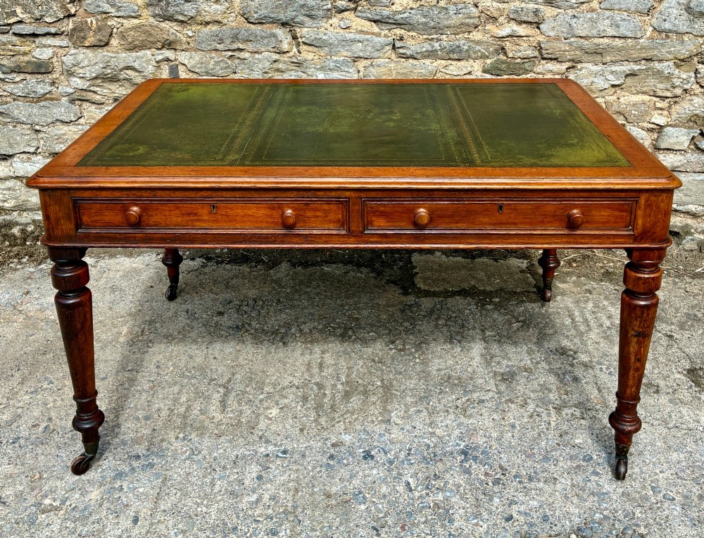 A Victorian oak writing desk featuring a green leather insert top, frieze drawers with wooden turned knobs, and turned legs with brass castors.