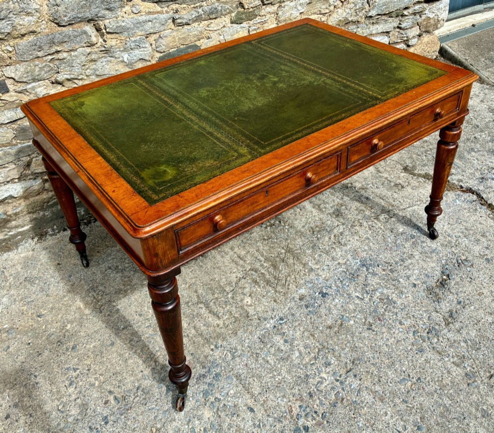 A Victorian oak writing desk featuring a green leather insert top, frieze drawers with wooden turned knobs, and turned legs with brass castors. View II